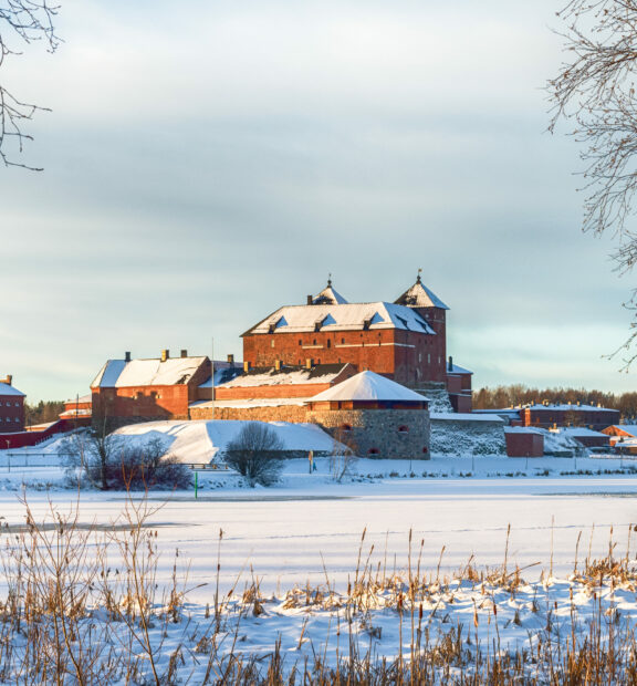 Jäätyneen ja lumen peitossa olevan järven rannalla sijaitseva punatiilinen Hämeen linna.