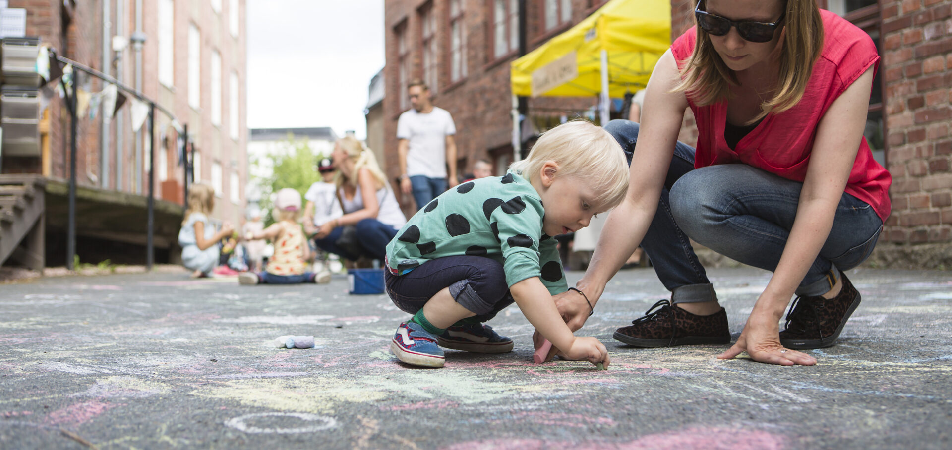Äiti piirtää lapsen kanssa kuvaa katuliiduilla