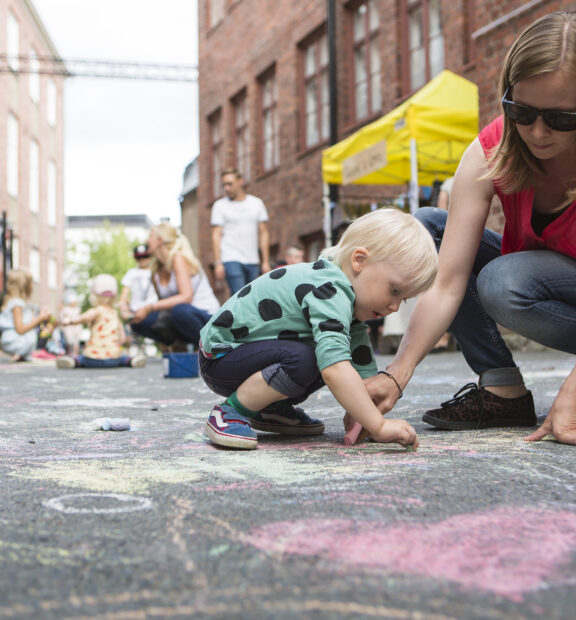 Äiti piirtää lapsen kanssa kuvaa katuliiduilla