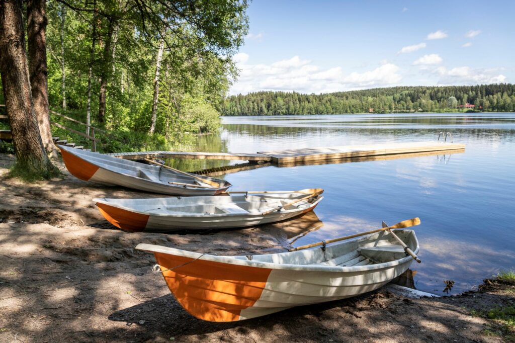 Järven rannalla kolme oranssi-valkoraidallista soutuvenettä