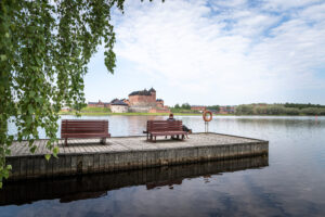 Järven rannalla oleva iso laituri, jossa kaksi penkkiä sekä pelastusrengas. Vastarannalla punatiilinen Hämeen linna.