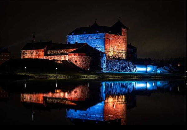 Värivaloilla valaistu punatiilinen Hämeen linna. 