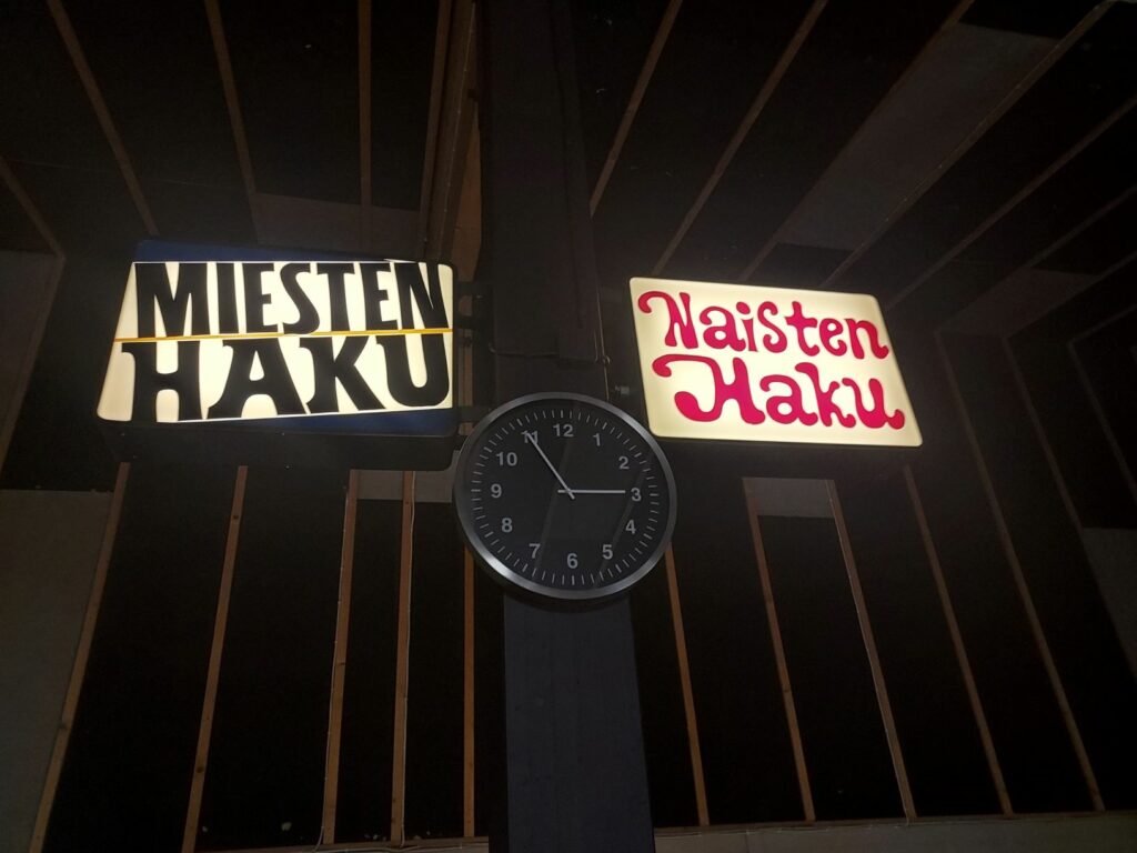 Seinäkello, jonka yläpuolella tekstit Miesten haku, Naisten haku.