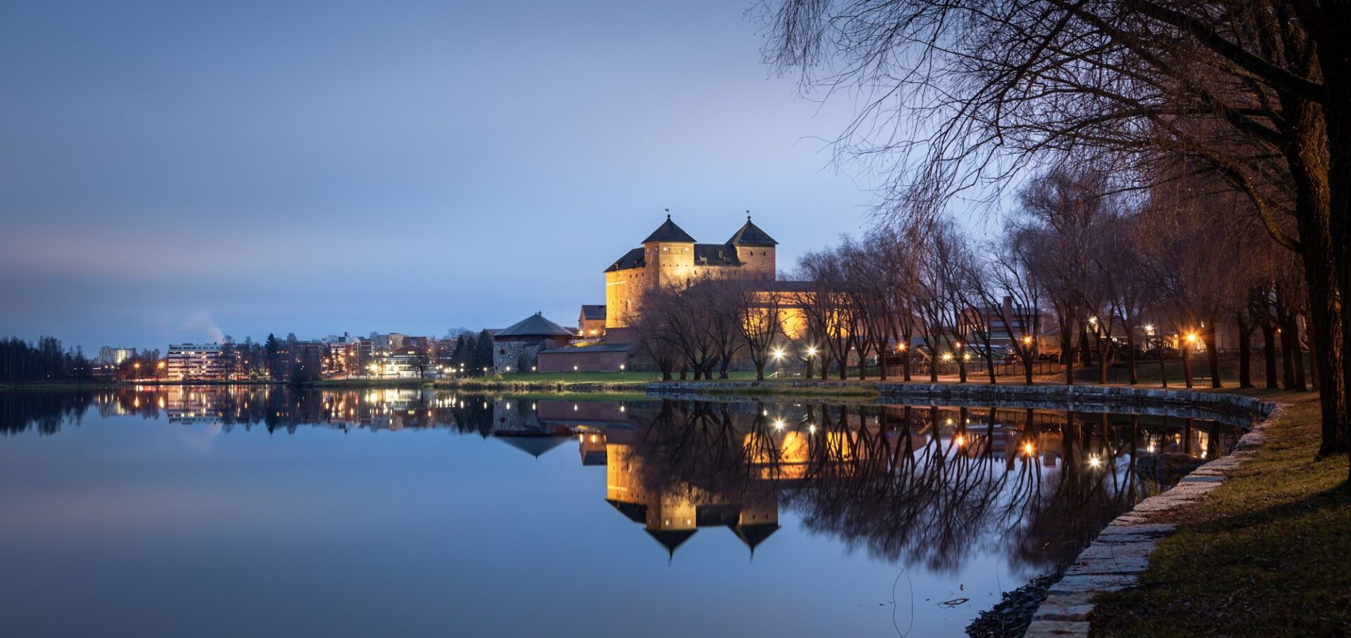 Järven rannalla sijaitseva Hämeen linnan kuvattuna vasten tummenevaa taivasta
