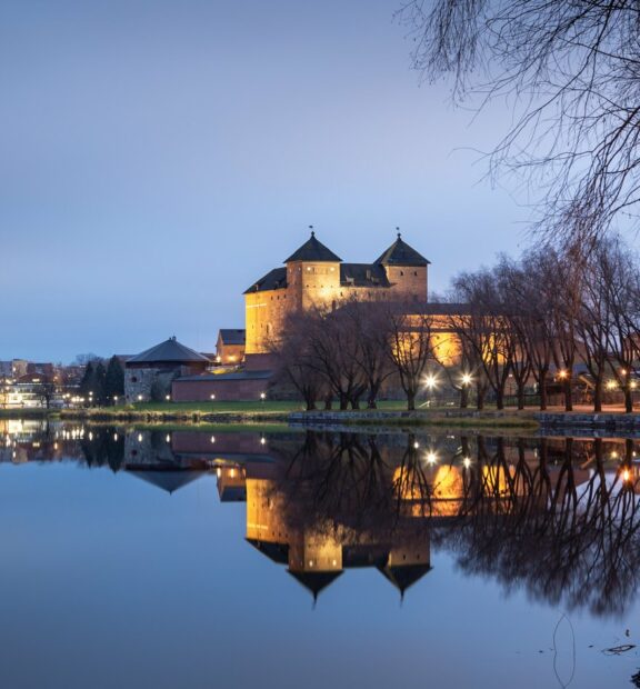 Järven rannalla sijaitseva Hämeen linnan kuvattuna vasten tummenevaa taivasta