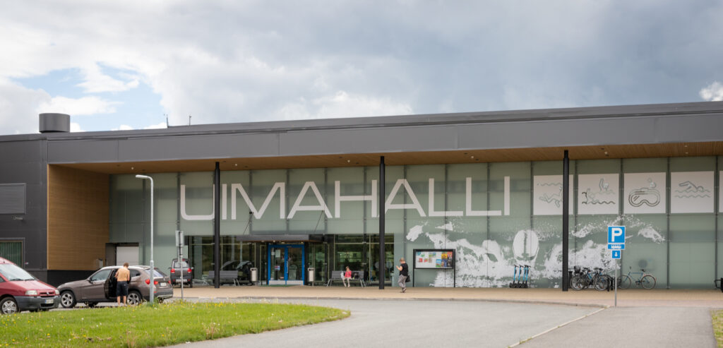 Uimahallin pääsisäänkäynti, jonka edessä on pysäköintialue.