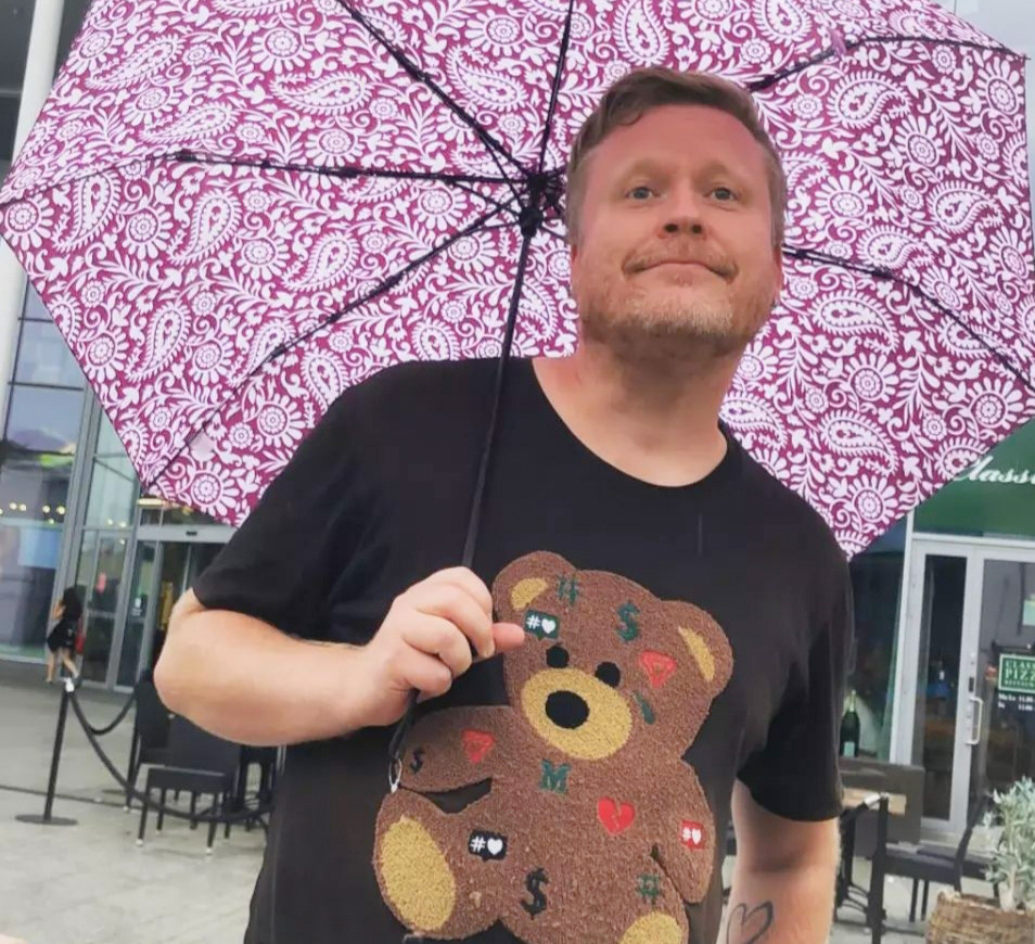Mies seisoo ulkona sateenvarjo kädessään. 