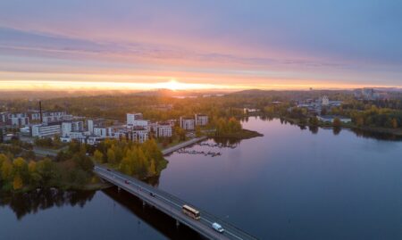 Aurinko nousee taivaanrannasta etualalla järvi jonka takana keskusta