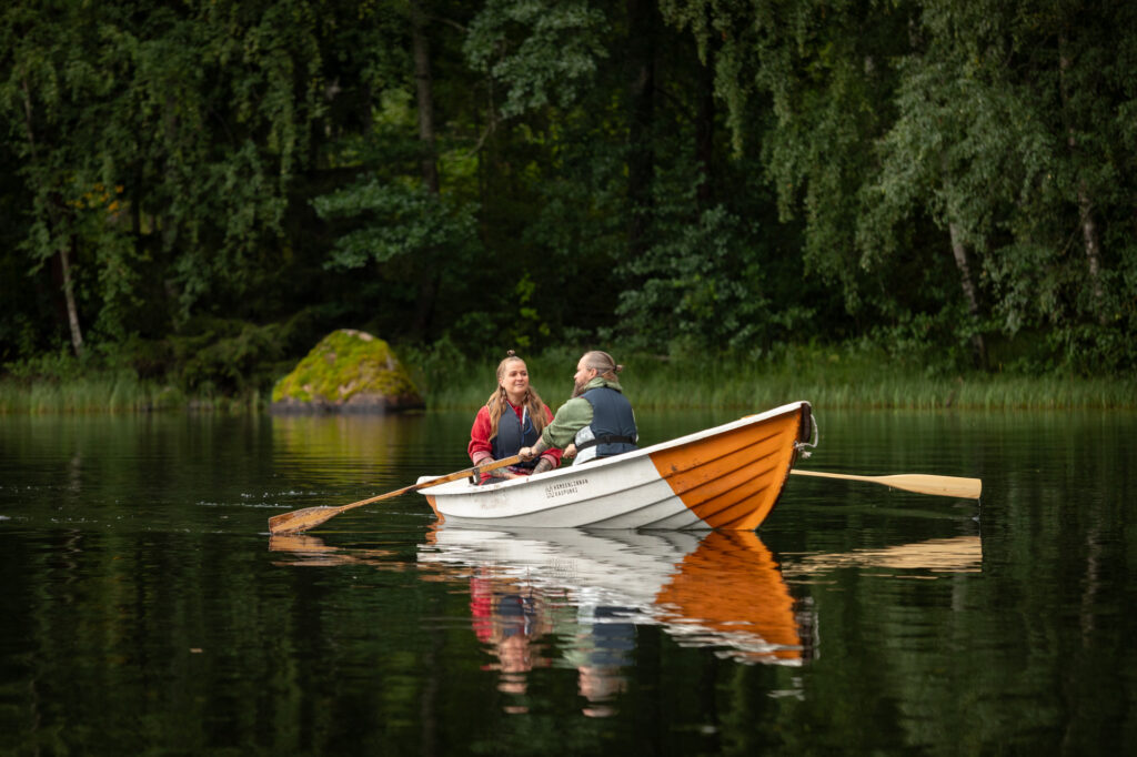 Mies ja nainen soutavat järvellä oranssi-valkoraidallisella veneellä.