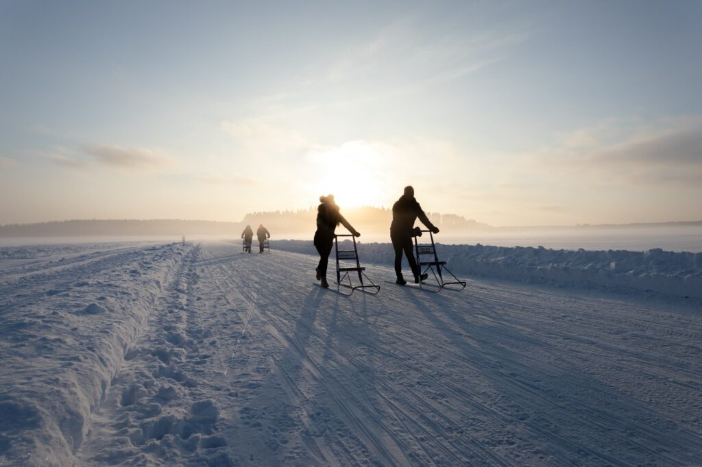 Neljä ihmistä potkukelkkailee laskevan auringon valossa järven jäällä