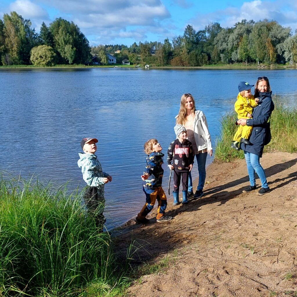 Kaksi naista ja neljä lasta seisoo järven rannalla.