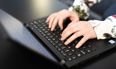 Kädet tietokoneella näpyttelee.