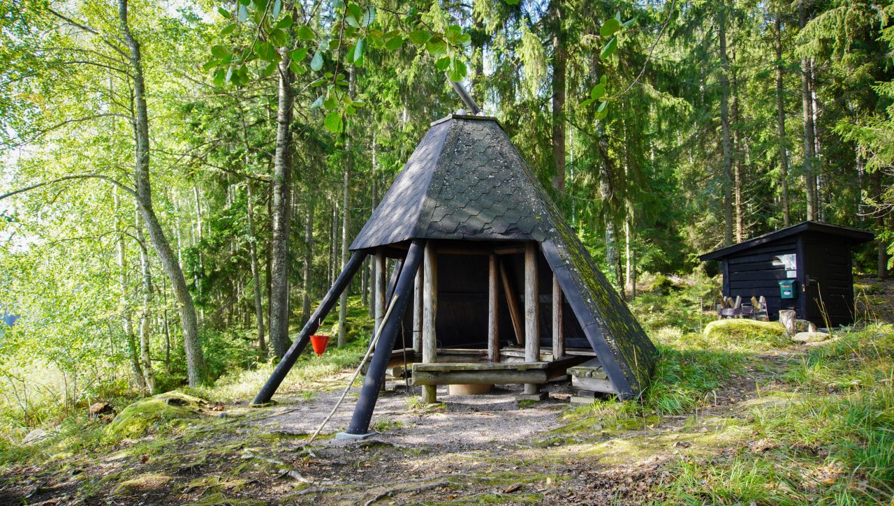 Large lean-to shelter hut painted black, with forest in the background.