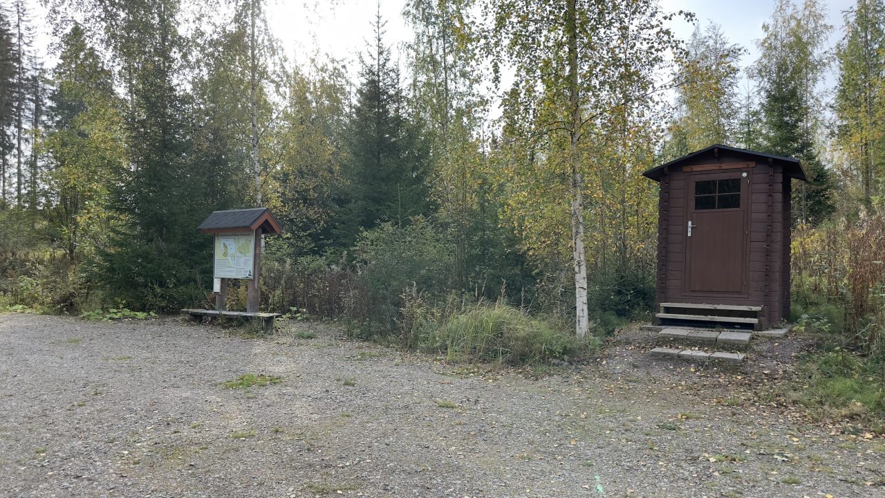 Infotaulu, joka on koivikkometsän edessä. Vieressä on puinen kuivakäymälä.