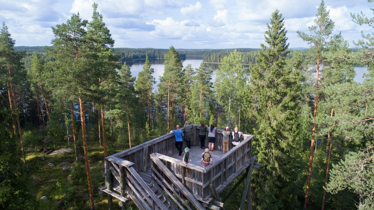 People in a high tower in the middle of the forest. They look at the lake landscape in front of them.