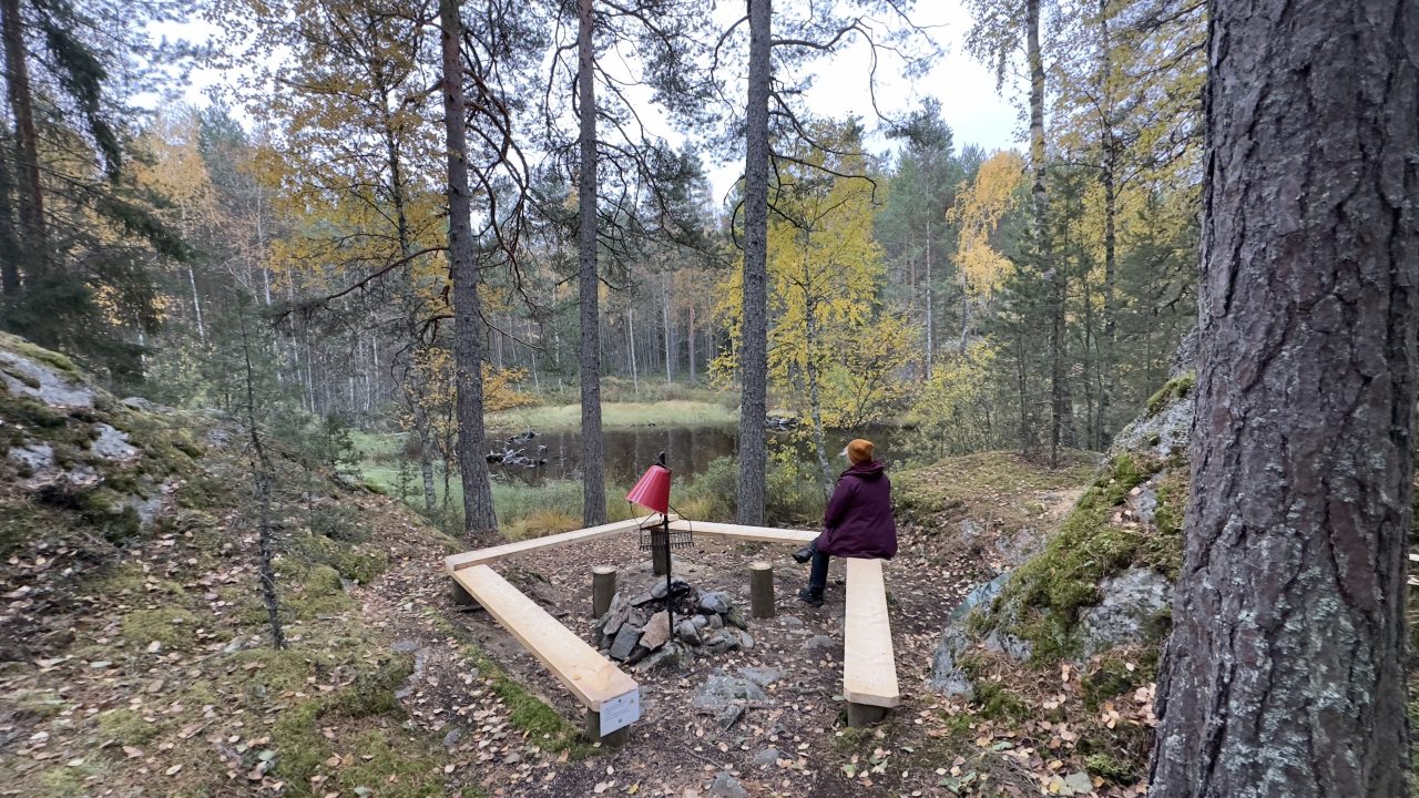 A woman sits by the campfire and looks out over the lake.