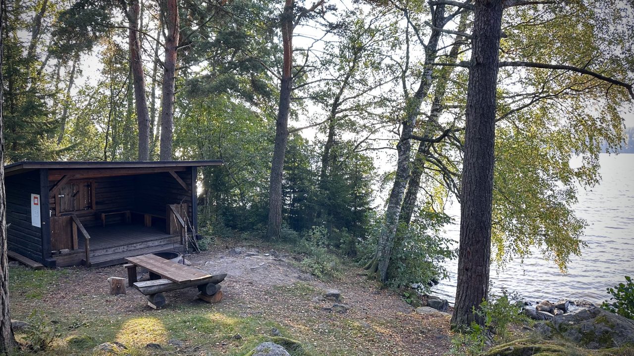 A dark, wooden lean-to shelter by the lake.