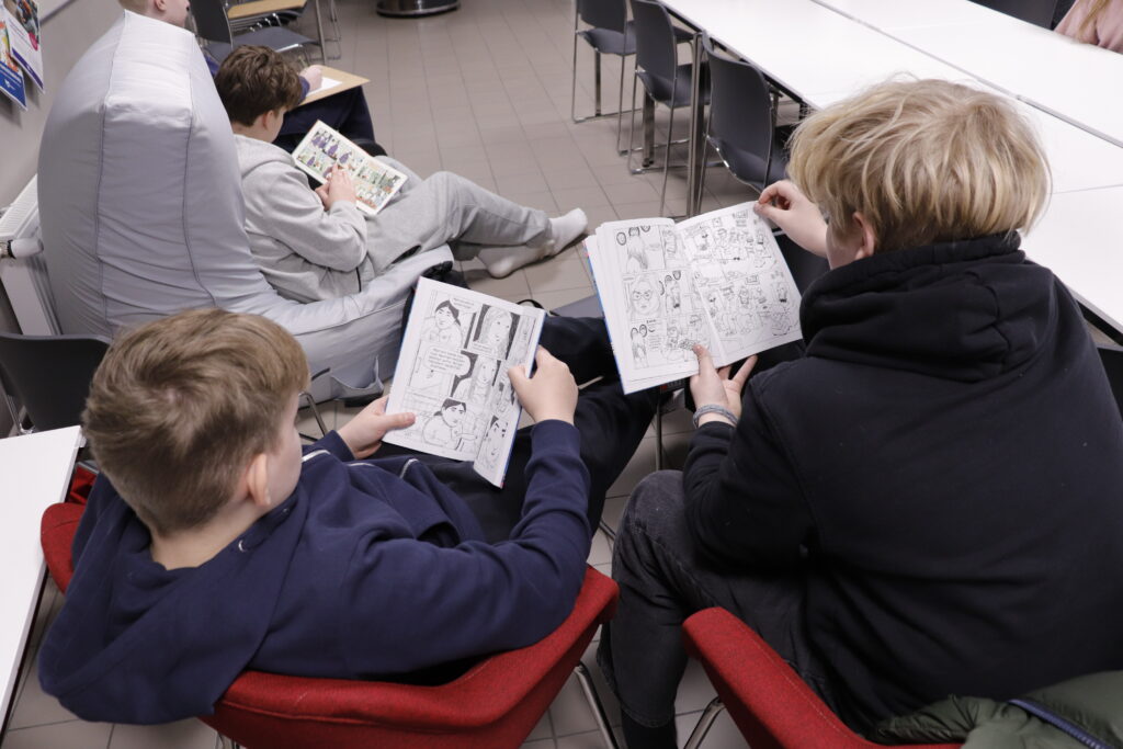 Kolme nuorta istuu nojatuoleissa ja lukee sarjakuvia