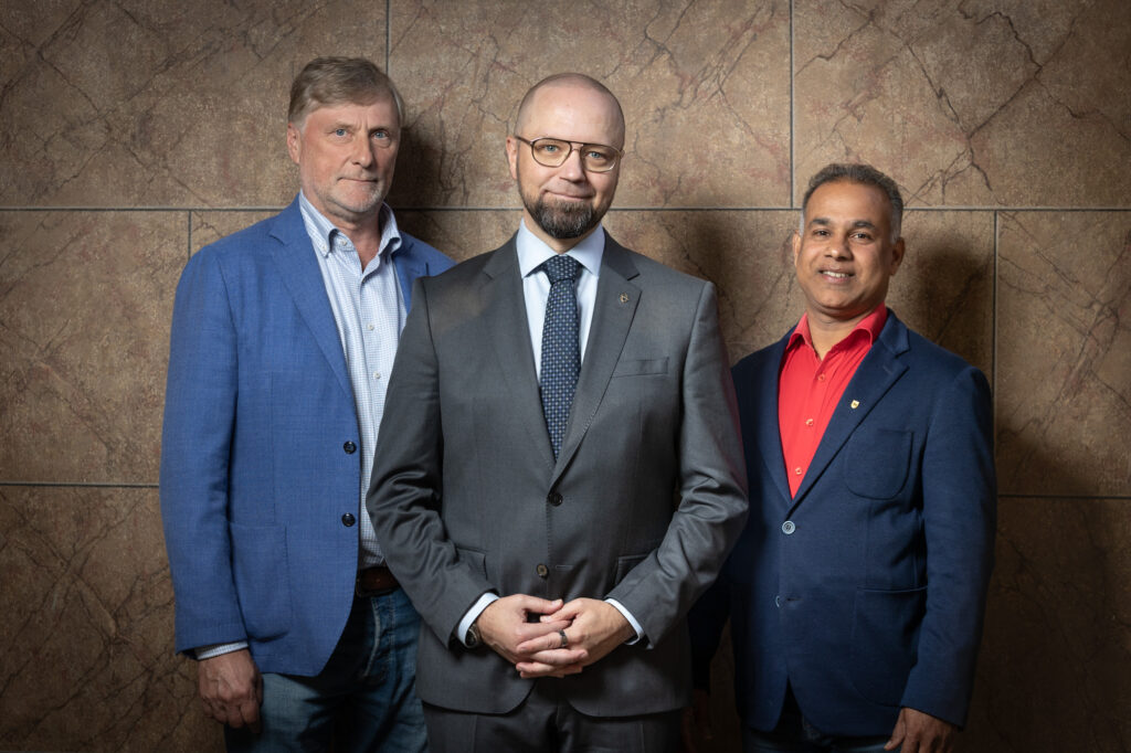 Kolme mieshenkilöä seisoo rinnakkain.