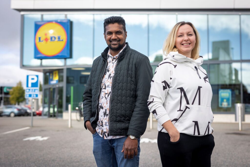 Kaksi henkilöä seisoo Lidlin myymälän edessä.