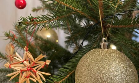 Kuusen oksilla roikkuvia joulupalloja ja oljesta tehtyjä tähtikoristeita.
