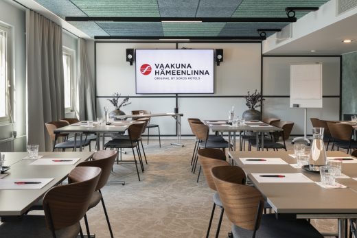 Meeting room before the start of a meeting. A television screen at the back of the room with the hotel logo and name.