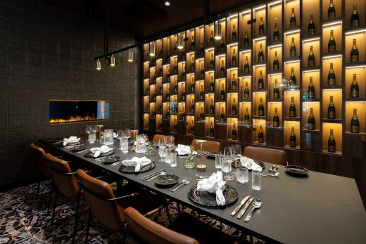 Restaurant hall in dim lighting. Table setting prepared on a dark row of tables. Illuminated bottles on the back wall.