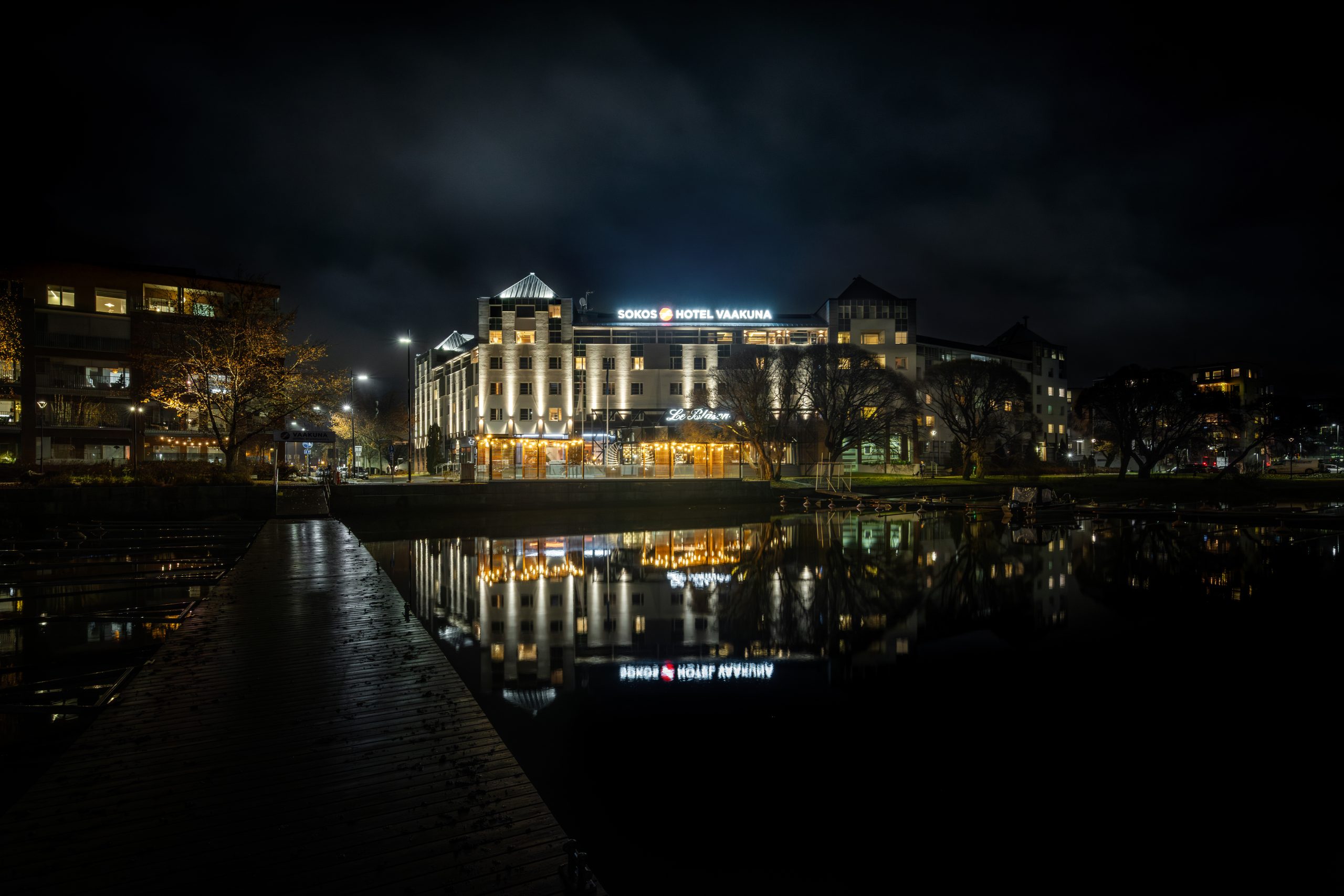The hotel on the shore of Lake Vanajavesi at night. The hotel lights are reflected on the water's surface. 