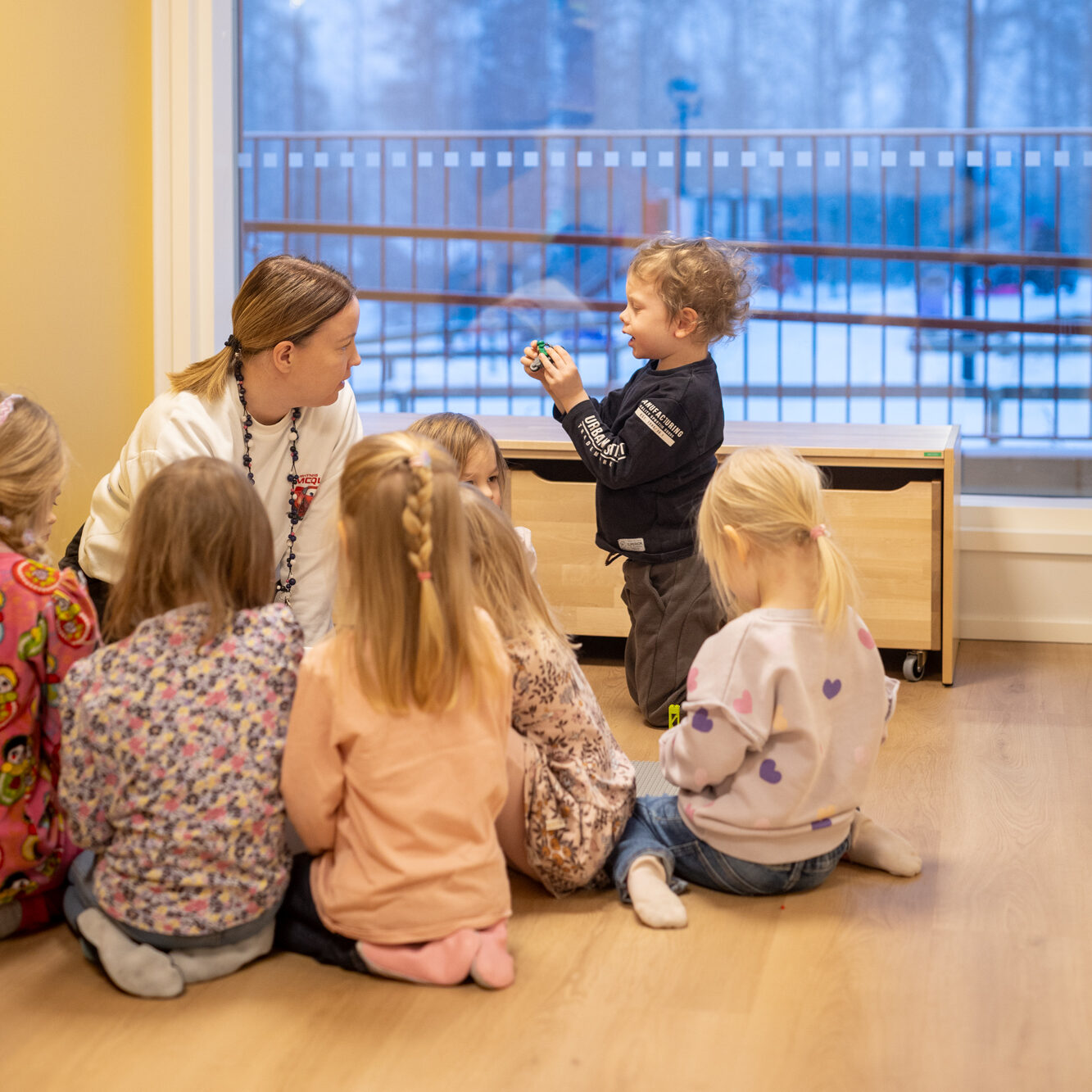 Päiväkodin työntekijä istuu lattialla lapsiryhmän kanssa.