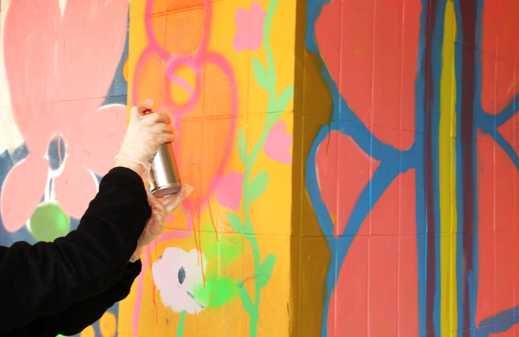 Käsi ja spraypullo, värikäs seinä