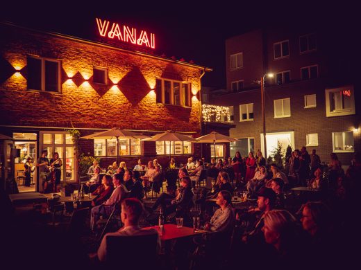 The area in front of Vanai in the evening. Many people on the terrace, with the building's lights shining.