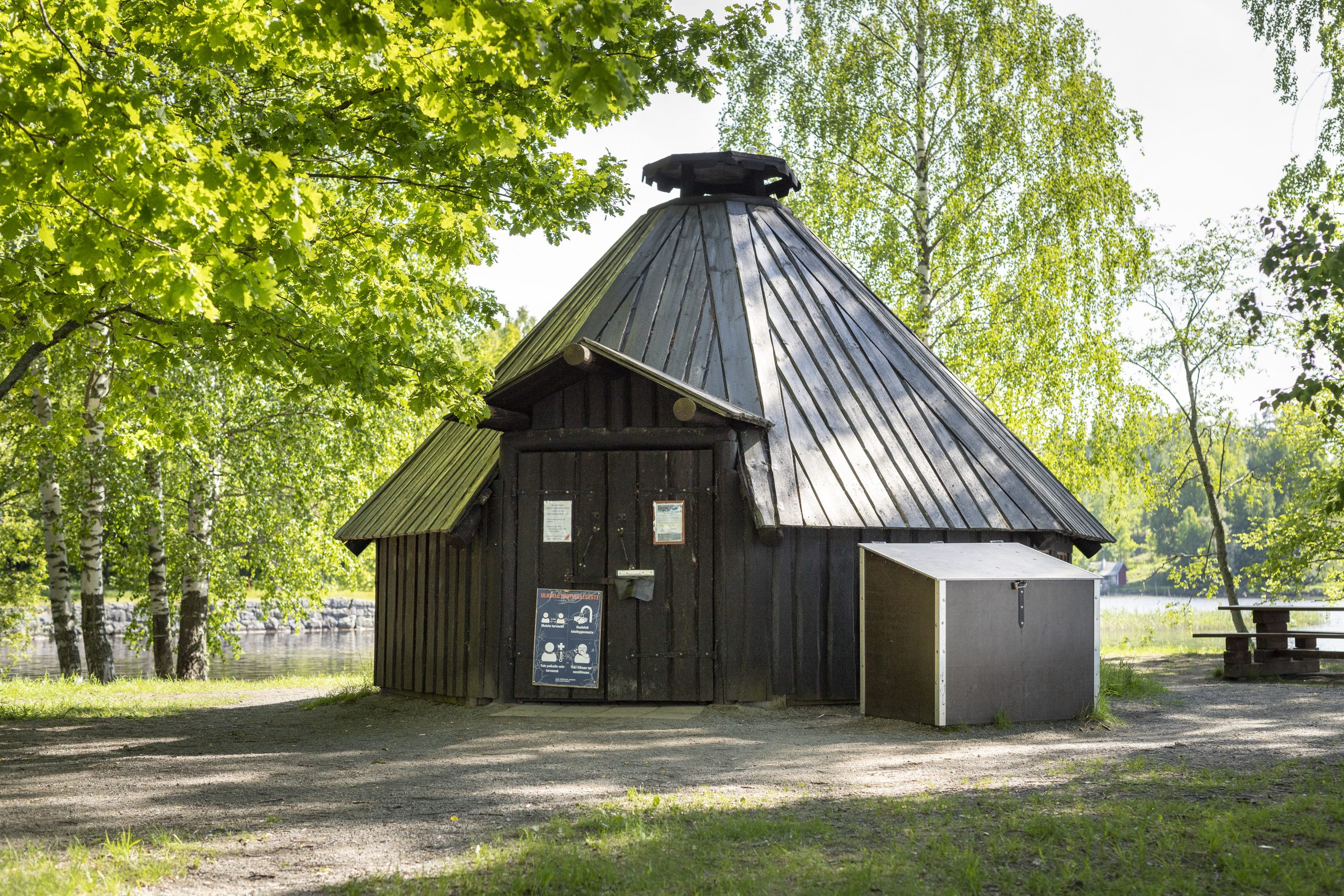 Aulangon tekosaarten vuokrakota, jonka kyljessä on puulaari ja vieressä pöytä.