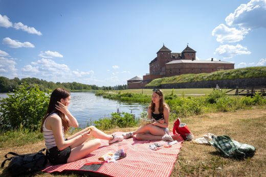 Kaksi nuorta nauttii piknikistä Hämeen Linnan edustalla.