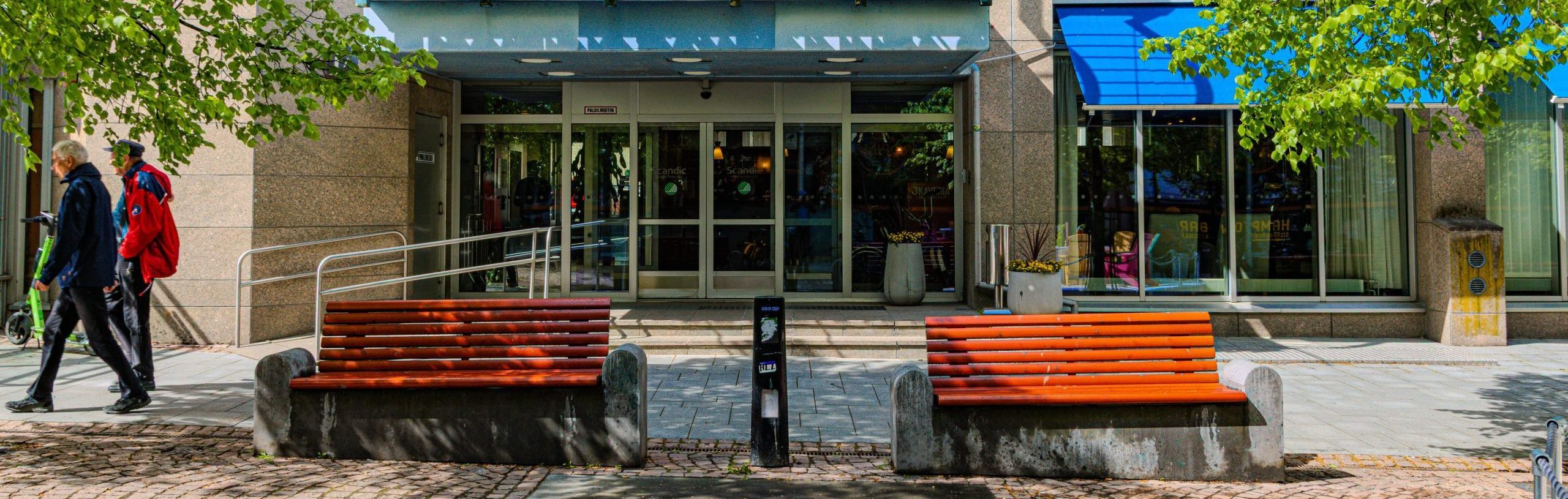 The front of the hotel with glass doors and two red wooden park benches in front.