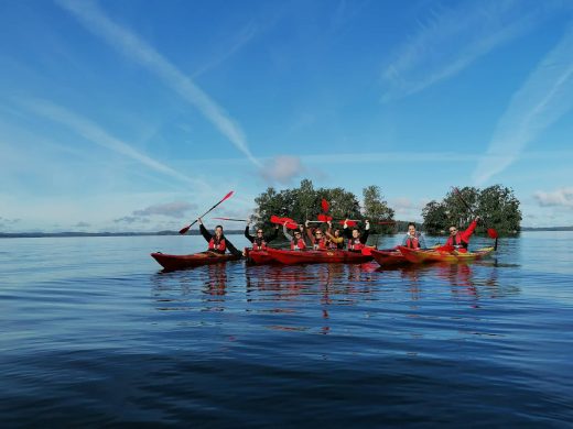 Five red kayaks side by side with people on the nearly calm Lake Vanajavesi in summer.