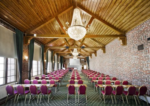 A large meeting room arranged in classroom style at Vanajanlinna. Chandeliers and burgundy chairs create a sophisticated atmosphere.