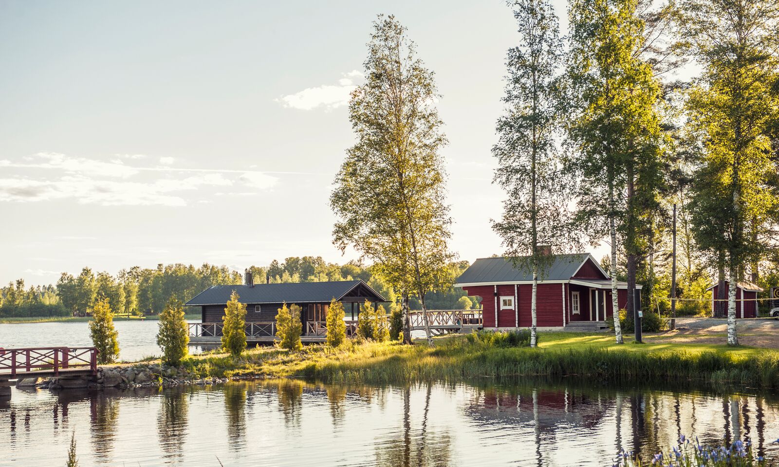 A red floating sauna in front of the lakeside sauna. Summer light and a calm lake view.