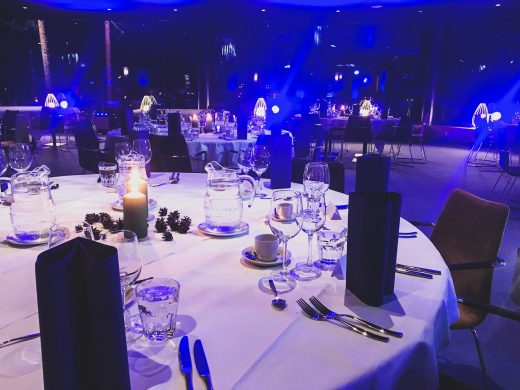 A dinner setting with white tablecloths and blue lighting in the room.