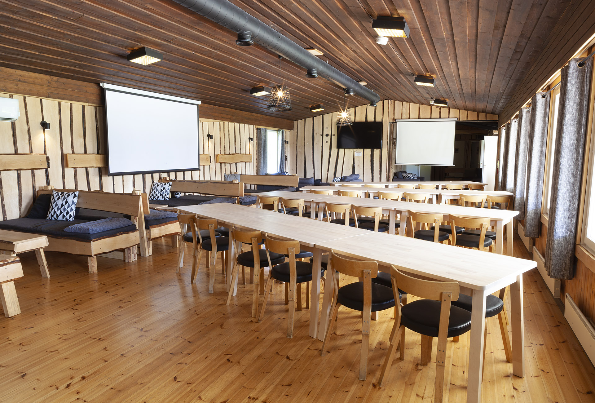 A meeting room with several long tables set up for a meeting. Whiteboards on two walls and a television screen at the back.