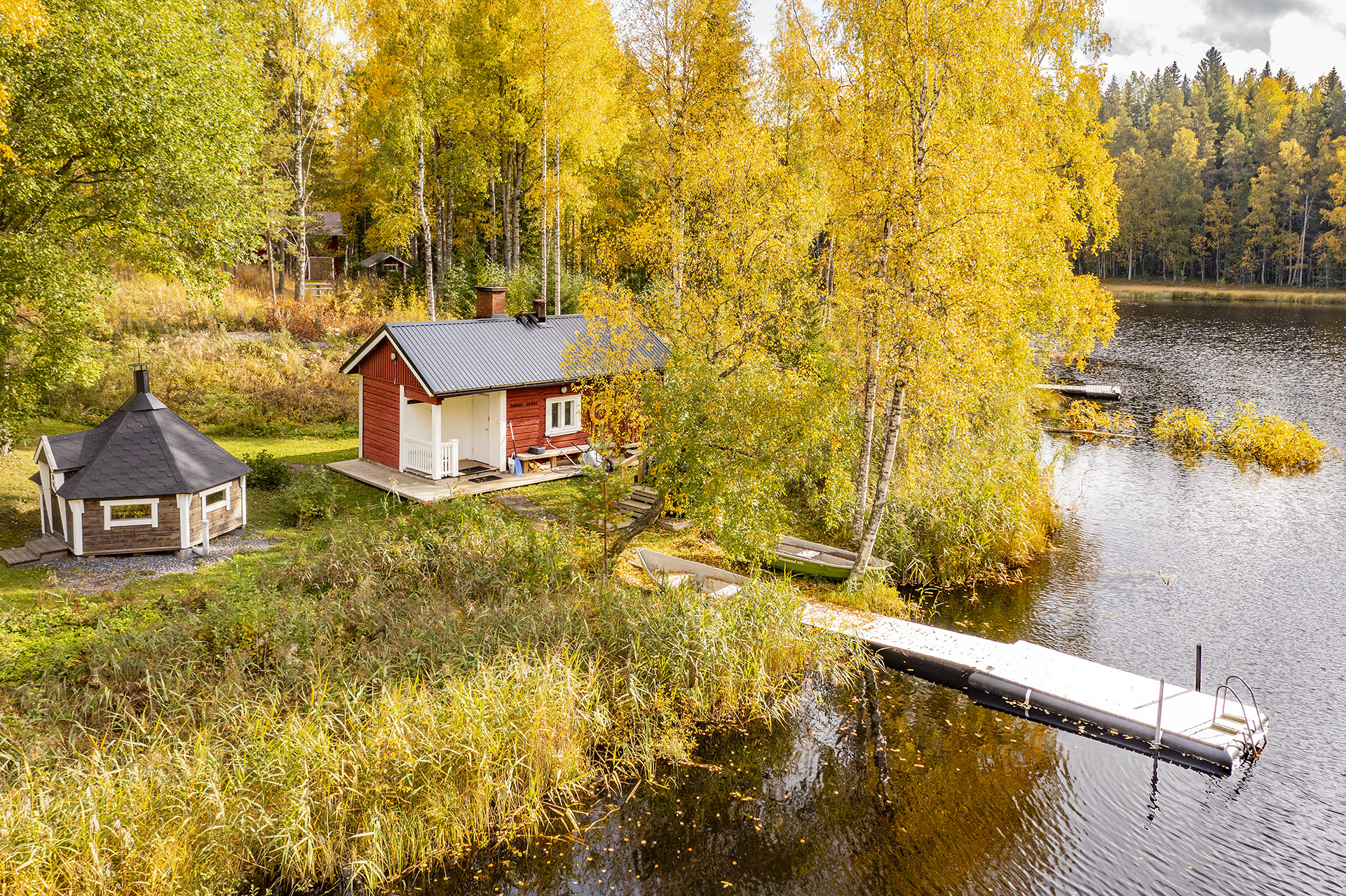 A red sauna building and a pier on the shore of an autumnal lake landscape.