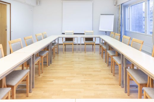 A meeting room with tables in a U-shape. A whiteboard and flipchart on the back wall.