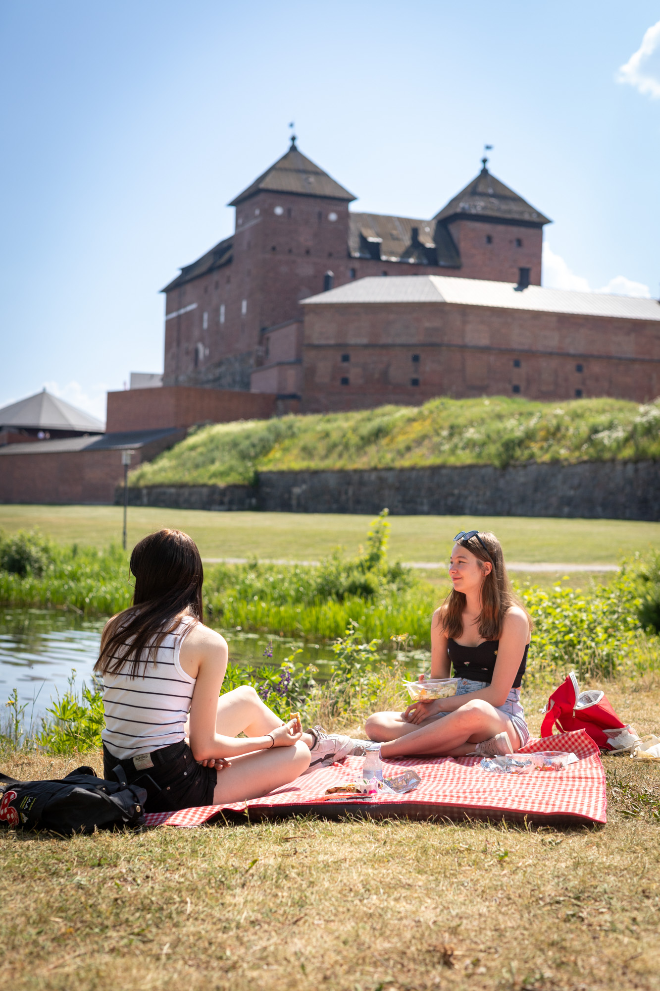 Two young people having a picnic in Linnanpuisto, with Häme Castle in the background.