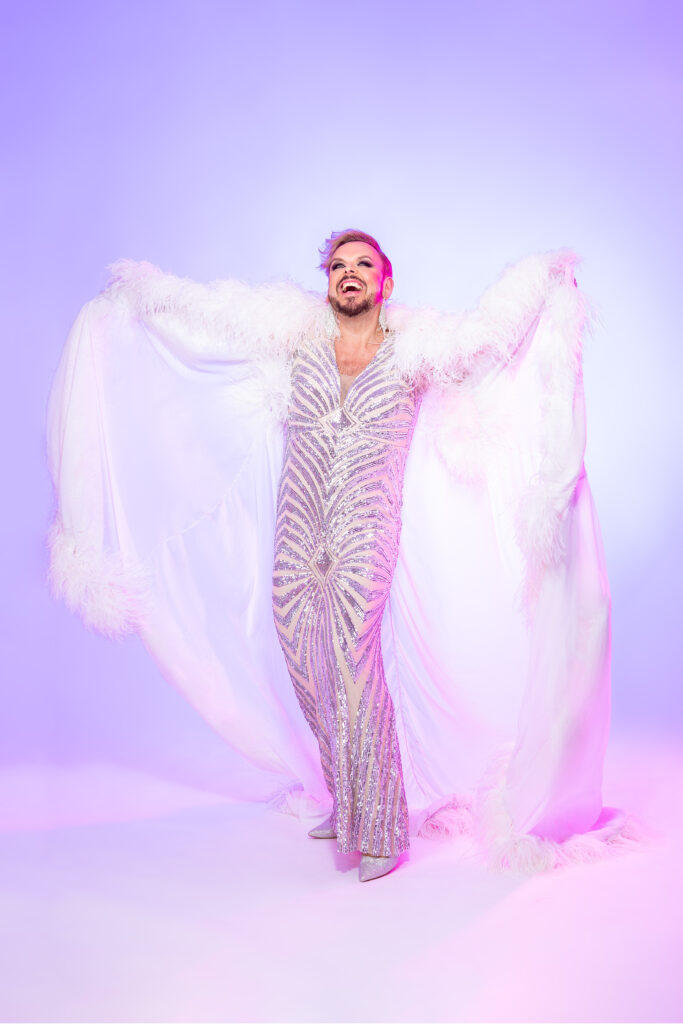 Glitterillä koristeltuun mekkoon ja höyhenviittaan pukeutunut drag-artisti.