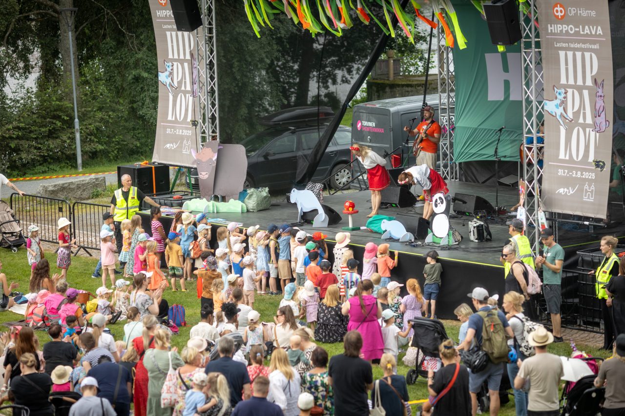 A view from the Hippalot outdoor stage. The performers take a bow, with a large audience of children gathered at the front of the stage.