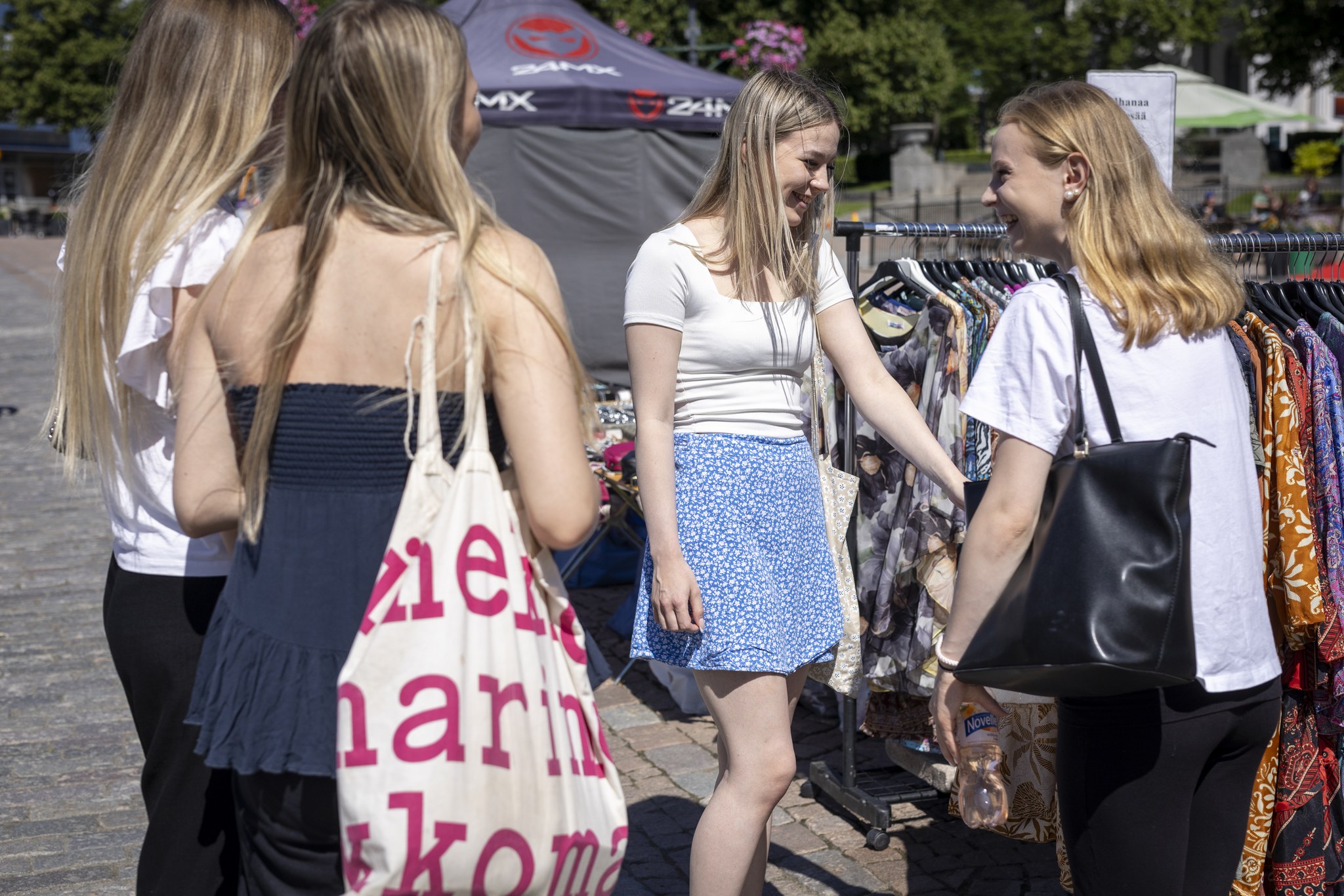 Neljä nuorta naista kiertelee torikojuja Hämeenlinnan torilla.