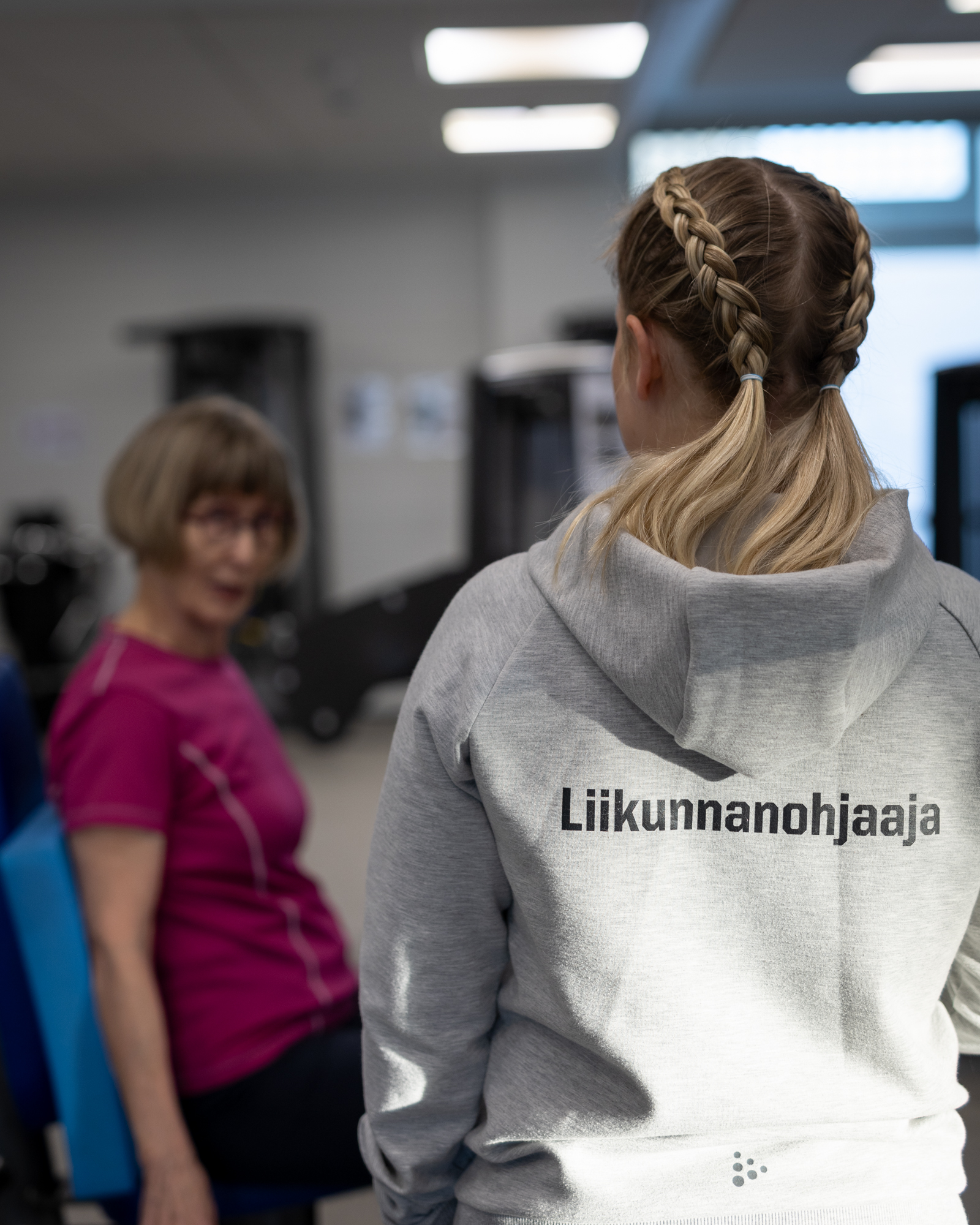 Liikunnanohjaaja ja kuntosalikävijä keskustelemassa.