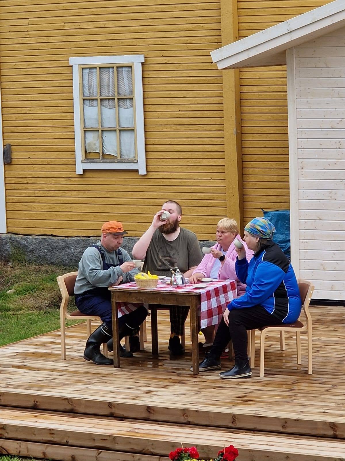 Ruuttanäyttämön esityksessä henkilöitä kahvipöydän ääressä.